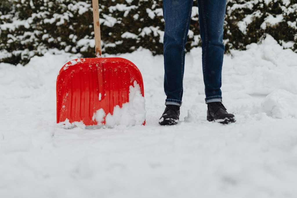 A person shoveling heavy winter snowfall using a red snow shovel. Outdoor winter scene.
